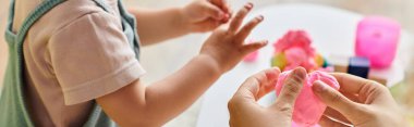 Kıvırcık saçlı anne, kucağında pembe bir nesneyle, evde Montessori eğitimini kucaklayan küçük kızlara rehberlik eder..