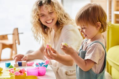 Kıvırcık bir anne ve küçük kızı evde Montessori eğitim metodunu uyguluyor, bir masada keşfediyor ve oynuyorlar..