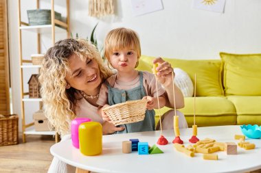 Kıvırcık saçlı bir anne ve küçük kızı evde Montessori metodunu araştıran bir sepetle neşeyle oynuyorlar..