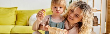 Kıvırcık bir anne bebeğini kucağına alıp evde Montessori eğitimi uygular..