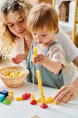 Kıvırcık saçlı bir anne ve küçük kızı Montessori metodunu uyguluyor, neşeyle inşa ediyor ve oyun oynuyorlar.