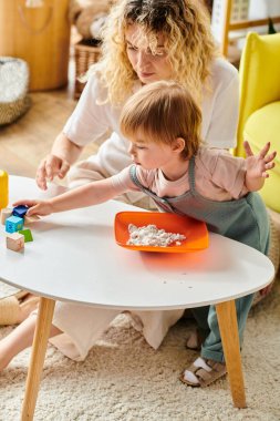 Kıvırcık saçlı bir anne, evde Montessori metodunu kullanarak küçük kızıyla şakacı bir şekilde iletişim kurar..