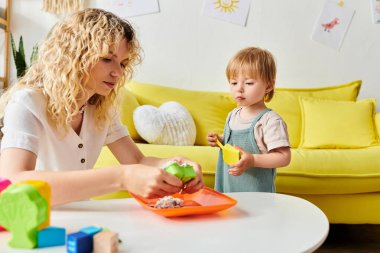 Kıvırcık bir anne, Montessori 'de küçük kızıyla rahat bir oturma odasında oyun oynar. Öğrenme ve kaynaşmayı teşvik eder..