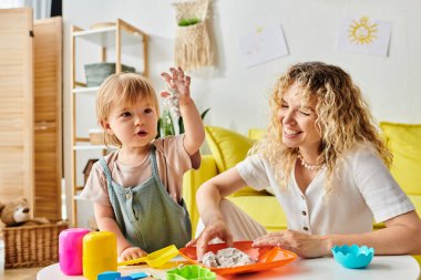 Kıvırcık bir anne ve küçük kızı bir masada Montessori eğitim seansına katıldılar..