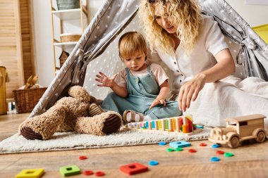 Kıvırcık anne ve küçük kızı rahat bir evde renkli bir oyun çadırında yaratıcı oyunlar oynuyorlar..