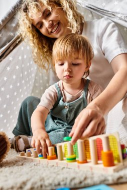 Kıvırcık bir anne ve küçük kızı evde renkli bloklarla oynayarak Montessori metodunu uyguluyorlar..