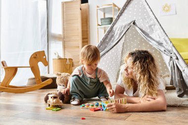 Kıvırcık saçlı bir anne ve küçük kızı, Montessori metodunu takip ederek, eğitici oyuncaklarla yaratıcı bir oyun oynuyorlar..