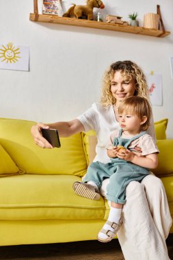 Kanepede oturan kıvırcık saçlı bir anne, küçük kızına şefkatle sarılıyor, sıcak ve sevgi dolu bir evde..