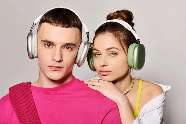 stock image A stylish young couple, deeply in love, wearing headphones and enjoying music together in a studio with a grey background.