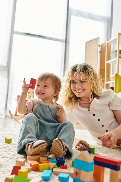 A curly-haired mother and her toddler daughter engage in educational play with blocks on the floor.