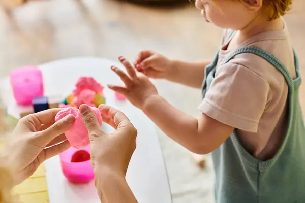 stock image mother guides her toddler daughters hand over a table, engaging in a Montessori education activity at home.