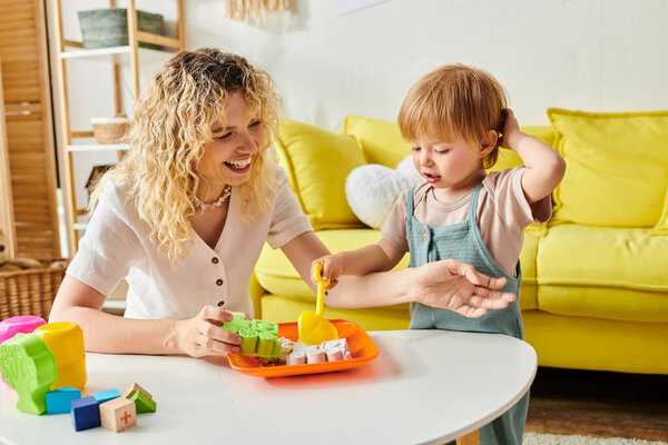 A curly-haired mother actively engages with her toddler daughter using Montessori method at a table.