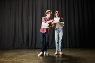 A stylish man and woman command attention in front of a black curtain. clipart