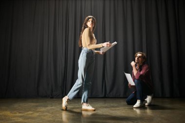 Woman standing gracefully in front of a black curtain during theater rehearsals next to her partner. clipart