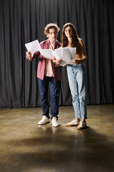 A man and woman pose elegantly against a black backdrop during theater rehearsals.