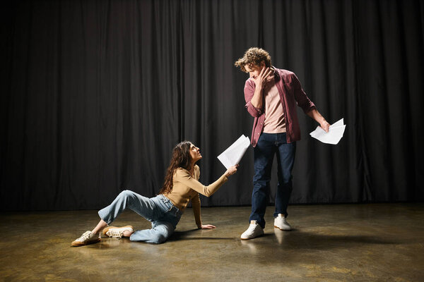 A man kneels next to a woman on the ground during theater rehearsals.