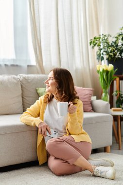 Orta yaşlı bir kadın bir fincan kahveyle yerde otururken huzur buluyor..