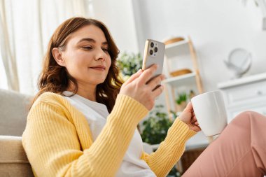 Orta yaşlı kadın kanepede rahat, akıllı telefon ekranına odaklanmış..