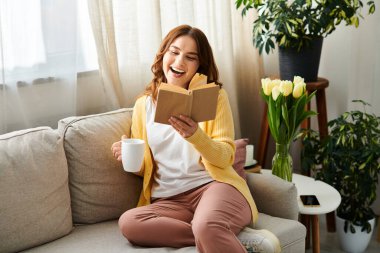 Middle aged woman engrossed in a book while seated on a cozy couch. clipart