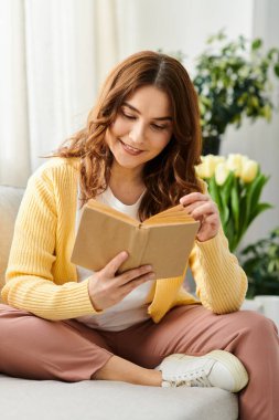 A middle-aged woman peacefully engrossed in reading while seated on a cozy couch. clipart