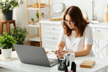 A middle-aged woman sitting at a table, engrossed in using a laptop computer. clipart