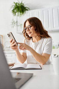 Orta yaşlı bir kadın cep telefonuyla bir masaya gömülmüş..