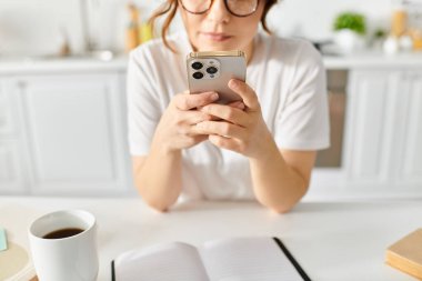 Orta yaşlı bir kadın ev masasında cep telefonuyla boğuşuyor..