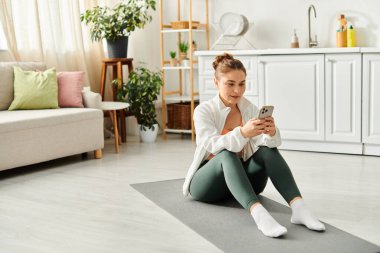 Yoga minderinde orta yaşlı bir kadın, akıllı telefona dalmış..