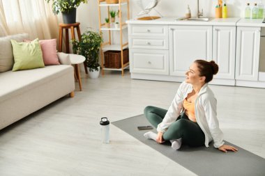 Orta yaşlı bir kadın oturma odasında yoga minderinde otururken huzur buluyor..
