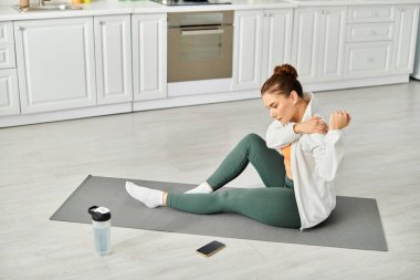 Middle aged woman finds peace on yoga mat in kitchen. clipart