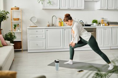 Orta yaşlı bir kadın evde yoga minderinde yoga pozu veriyor..
