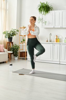 Beyaz gömlekli orta yaşlı bir kadın evde yoga yapıyor..