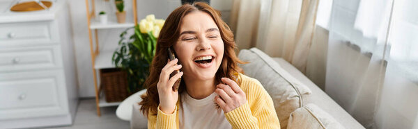 A middle-aged woman sitting on a couch, talking on a cell phone.