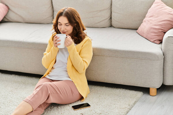 A middle-aged woman sitting on the floor, peacefully holding a cup of coffee.