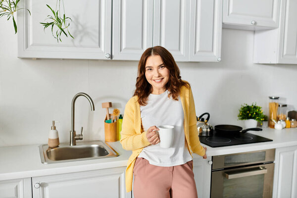 Middle-aged woman standing in kitchen, holding a cup.