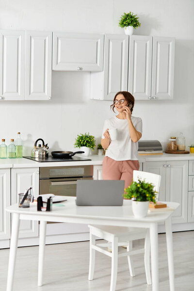 Middle-aged woman conversing on cell phone in home kitchen.