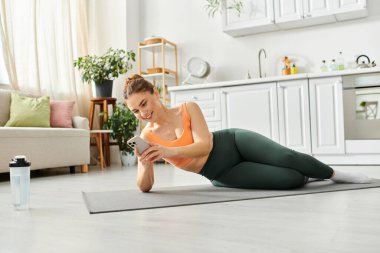 Middle aged woman balances in yoga pose on mat at home. clipart