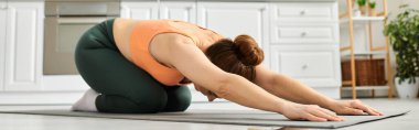 Orta yaşlı bir kadın paspasın üzerinde nazikçe yoga pozu veriyor..