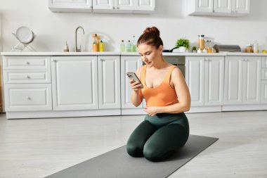 Orta yaşlı bir kadın yoga minderinde akıllı telefonu kontrol ediyor..