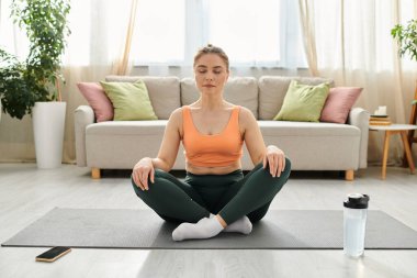 Orta yaşlı bir kadın oturma odasındaki yoga minderinde huzur buluyor..