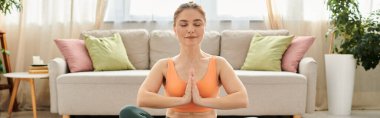 Middle-aged woman gracefully performs yoga in front of a couch. clipart