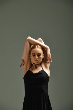 Siyah elbiseli genç ve güzel bir balerin elleri başının üstünde poz veriyor..