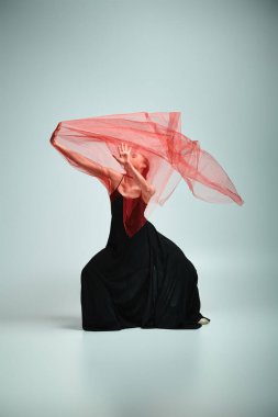 Siyah elbiseli zarif bir balerin başının üstünde kırmızı bir peçeyle zarif bir şekilde hareket eder..