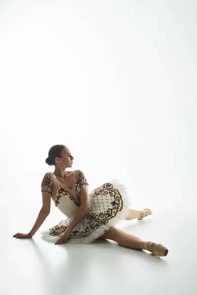 stock image A young, beautiful ballerina in a dress sits gracefully on the floor.