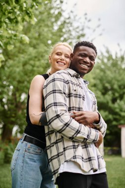 Afrika kökenli Amerikalı bir erkek ve beyaz bir kadın çimlerin üzerinde birlikte duruyor, doğayla ve birbiriyle bağ kuruyor..