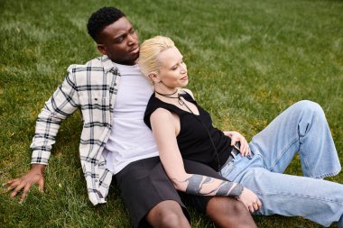 A multicultural couple, an African American man, and a Caucasian woman, laying contently on the grass in a park. clipart