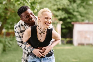 An African American man tenderly holds a Caucasian woman in a loving embrace amidst the serene surroundings of a park. clipart