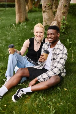 A happy, multicultural couple, an African American man and a Caucasian woman, sitting together on the grass in a park. clipart