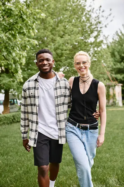 stock image A happy multicultural couple, an African American man and Caucasian woman, standing together in the lush green grass of a park.