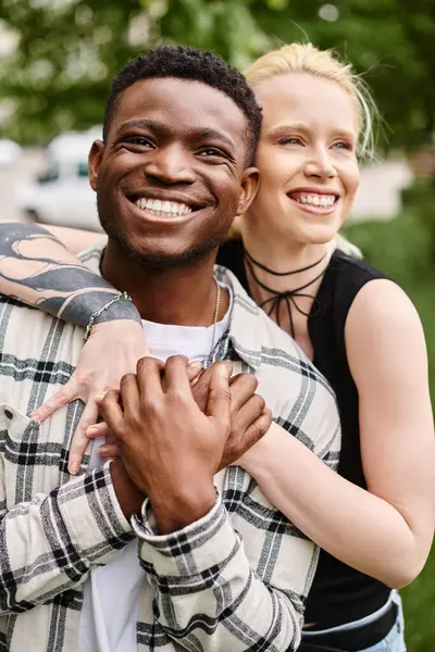 A happy multicultural couple - an African American man holding a Caucasian woman in his arms - in a romantic embrace outdoors in a park.